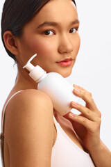 Asian woman holds a white pump bottle in a clean studio setting, smiling softly as she presents...