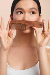 asian woman holds a wooden comb near her face in a closeup portrait, playful expression, soft...