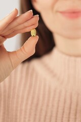 Close-up of an unrecognizable smiling woman holding a collagen capsule beauty supplement. Concept of skincare, anti aging, self care and daily wellness routine.