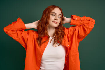 Young woman showcases vibrant autumn fashion with a playful pose on a green backdrop