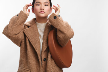 asian woman wearing a cozy beige coat stands against a plain backdrop, posing confidently as a...