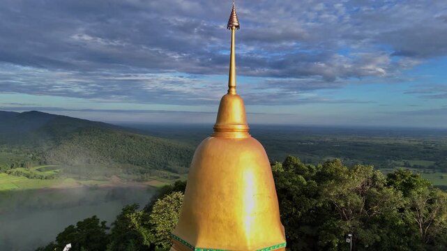 Beautiful 4K aerial footage of the golden pagoda atop a mountain at Wat Pa Tham Makluea in Sakon Nakhon, Thailand. Stunning drone view of a serene temple and new scenic viewpoint.