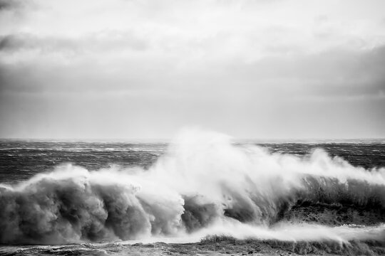 Dramatic black and white image of a huge ocean wave crashing with force