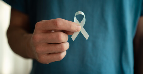 Close up of a young man holding a blue ribbon in his hand. Symbol of prostate cancer awareness,...
