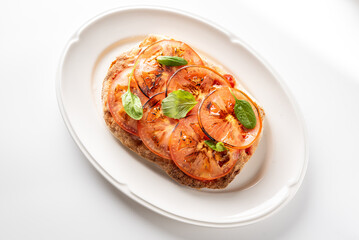 An Italian bruschetta appetizer on a white plate, featuring toasted bread topped with sliced tomatoes, fresh basil leaves, and a glossy balsamic glaze drizzle