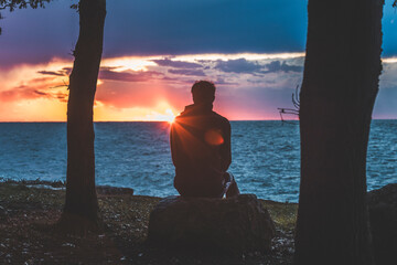 sunset over the sea in istria, croatia, with waves, dramatic purple clouds, the sun right on the horizon and the silhouette of a person looking the panorama