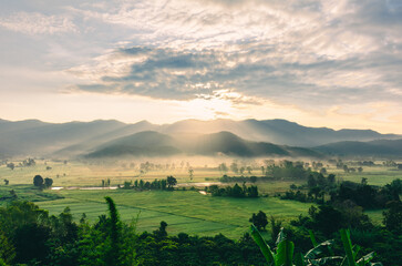 The beautiful landscape of the sunrise, The sun's rays through the clouds at the top of the hill and the Rice fields Faint fog, Chiang Rai Thailand