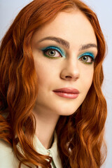 Naklejka premium A young redhead woman poses confidently, highlighting her vibrant makeup in a studio