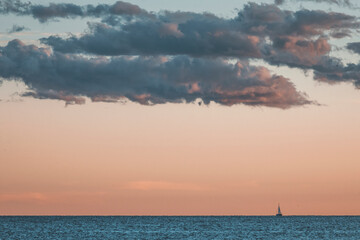 sunset over the sea in istria, croatia, with pastel pink clouds and a small sailing boat in the water