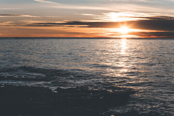 sunset from the cape in porec, croatia, with waves on the water and orange sky
