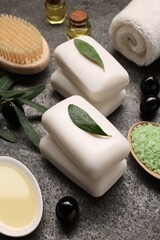 Olive soap bars, oil, sea salt and other bath accessories on gray textured table, closeup