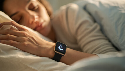 Close-up of a woman sleeping peacefully in bed with a smartwatch on her wrist displaying a sleep mode icon, bathed in soft warm morning light creating a calm and cozy mood