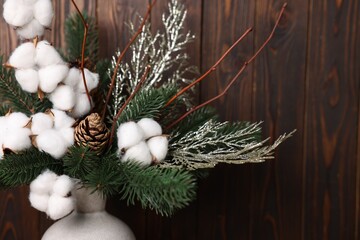 Beautiful composition with fir tree branches in vase near wooden wall indoors, closeup. Winter decor