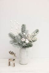 Beautiful composition with fir tree branches in vase and reindeer figure on white table indoors. Winter decor