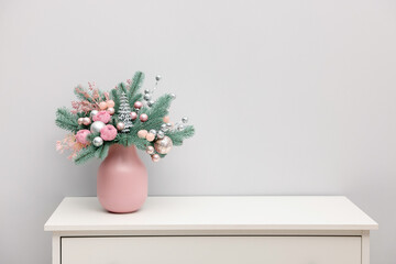Beautiful composition with fir tree branches in vase on white chest of drawers near light wall indoors, space for text. Winter decor