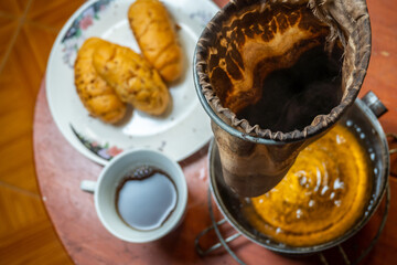 My hand holding a porcelain plate and glass with coffee and bread in front of the window, appreciating the sunset. Mano sosteniendo un plato de porcelana y un vaso con café y pan frente a la ventana.