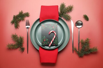 Christmas setting with plates, cutlery and fir tree branches on red background, flat lay