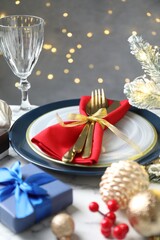 Festive table setting with Christmas decor on light marble background against blurred lights, closeup