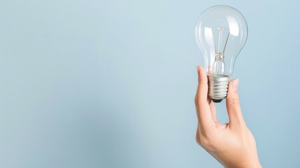 Hand Holding Clear Light Bulb Against Light Blue Background