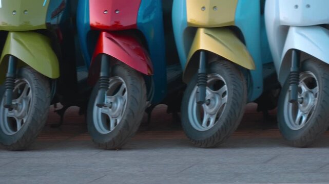 A close-up of front wheels of colorful scooters (motorbikes) parked in line on the road in Siem Reap, Cambodia