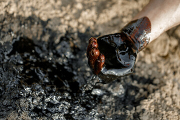 Close-up of a hand covered in dark oil, reaching out towards a slick surface, showcasing the impact of industrial pollution and environmental concerns in a natural setting