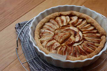 Traditional french cake Tart aux pommes with sliced apples on a cooling rack on wooden table