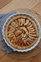 Traditional french cake Tart aux pommes with sliced apples on a cooling rack on wooden table