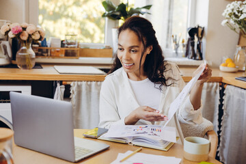 Professional businesswoman using laptop, working at home in kitchen showing graphs having video call