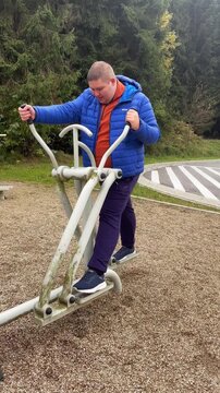 Young overweight man doing exercises on outdoor exercise machines