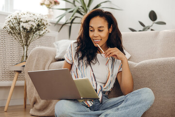 Positive, African American woman student using laptop working at home in living room