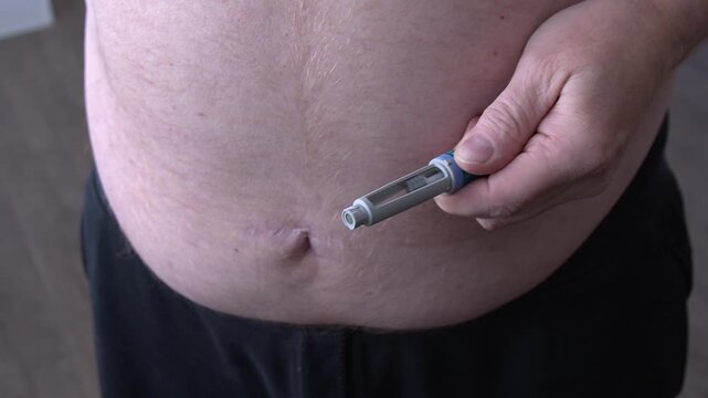 Fat man prepares to add needle to medication injector pen, large belly