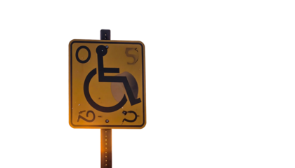 Yellow accessible sign illuminated in dark, depicting a person in wheelchair for disability access