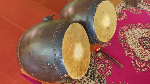 Two antique Taiko drums with leather membranes stand in a Buddhist temple. Shot in motion