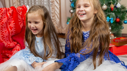 A happy little girls in a beautiful blue dress sitting in festive Christmas interior with a gifts and cheerful laughing.