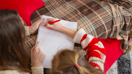 Cute little girl with mom writing making checklist sitting on floor in decorated living room