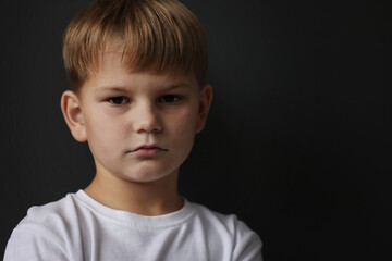 Upset little boy on black background, space for text
