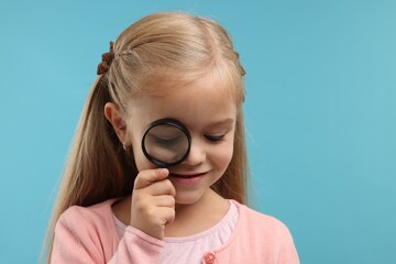 Little girl with magnifying glass on light blue background