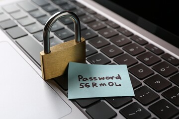 Paper note with password and closed padlock on laptop, closeup