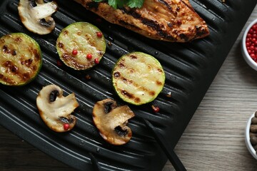 Electric grill with tasty chicken fillet, mushrooms, spices and zucchini on wooden table, flat lay