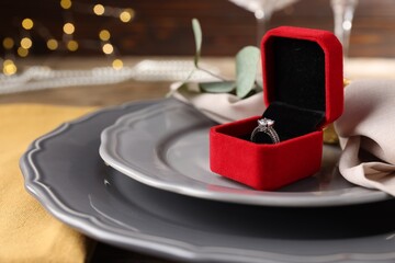 Romantic dinner. Box with engagement ring, napkin and plates on table, closeup