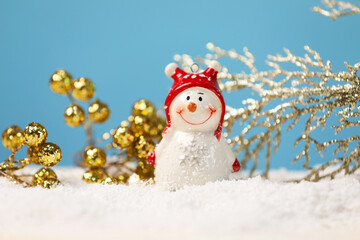 Cute decorative snowman and branches on artificial snow against light blue background, closeup