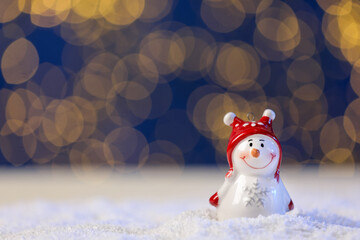 Cute decorative snowman on artificial snow against blue background with blurred lights, closeup. Space for text