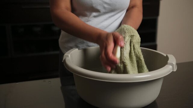 Woman's Hands Washing a Green Towel with Soap in a Basin, Emphasizing Cleanliness