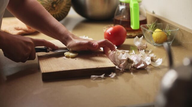 Hands Crushing Fresh Garlic Cloves on a Cutting Board in a Home Kitchen