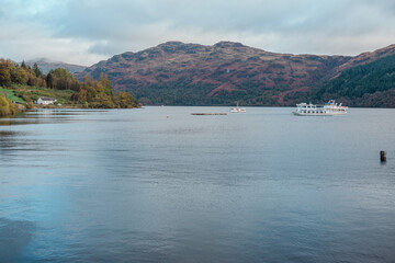 Tarbet, United Kingdom - October 11 2025: A beautiful, panoramic photograph of the historic Tarbet extending into the tranquil waters of Loch Lomond, featuring vibrant autumn foliage, Scotland.