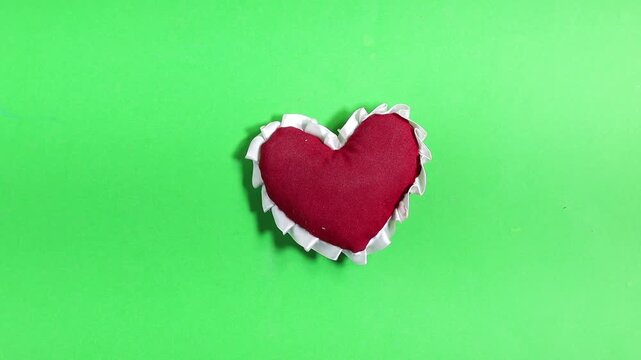 Hand Holding a Red Heart-Shaped Pillow Against a Vivid Green Background