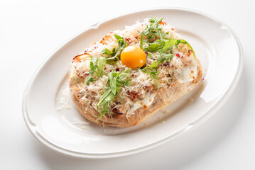 An elegant single serving pizzetta topped with creamy cheese, fresh arugula, shredded crab meat, and a bright raw egg yolk on an oval white plate on a white surface