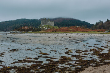 A dramatic and atmospheric photograph of the ruined medieval Castle Tioram (pronounced "Cheerum"), the former stronghold of the Clanranald branch of the MacDonalds - in Loch Moidart