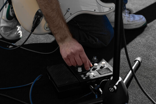 Musician adjusting electric guitar pedalboard during outdoor performance, foot, finger pressing effect pedal and instrument cable, creative live concert stage setup, modern music gear, sound control