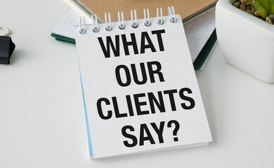 A white spiral notebook with the words What Our Clients Say written on it.